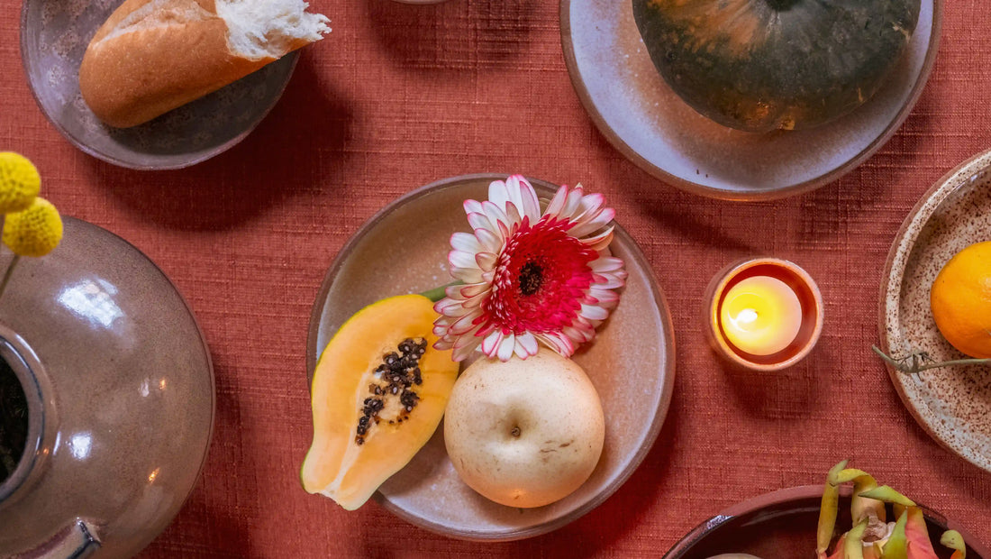 Beautiful ceramics and fruit are displayed across a red tablecloth advertising the new collaboration where dinners and ceramics meet